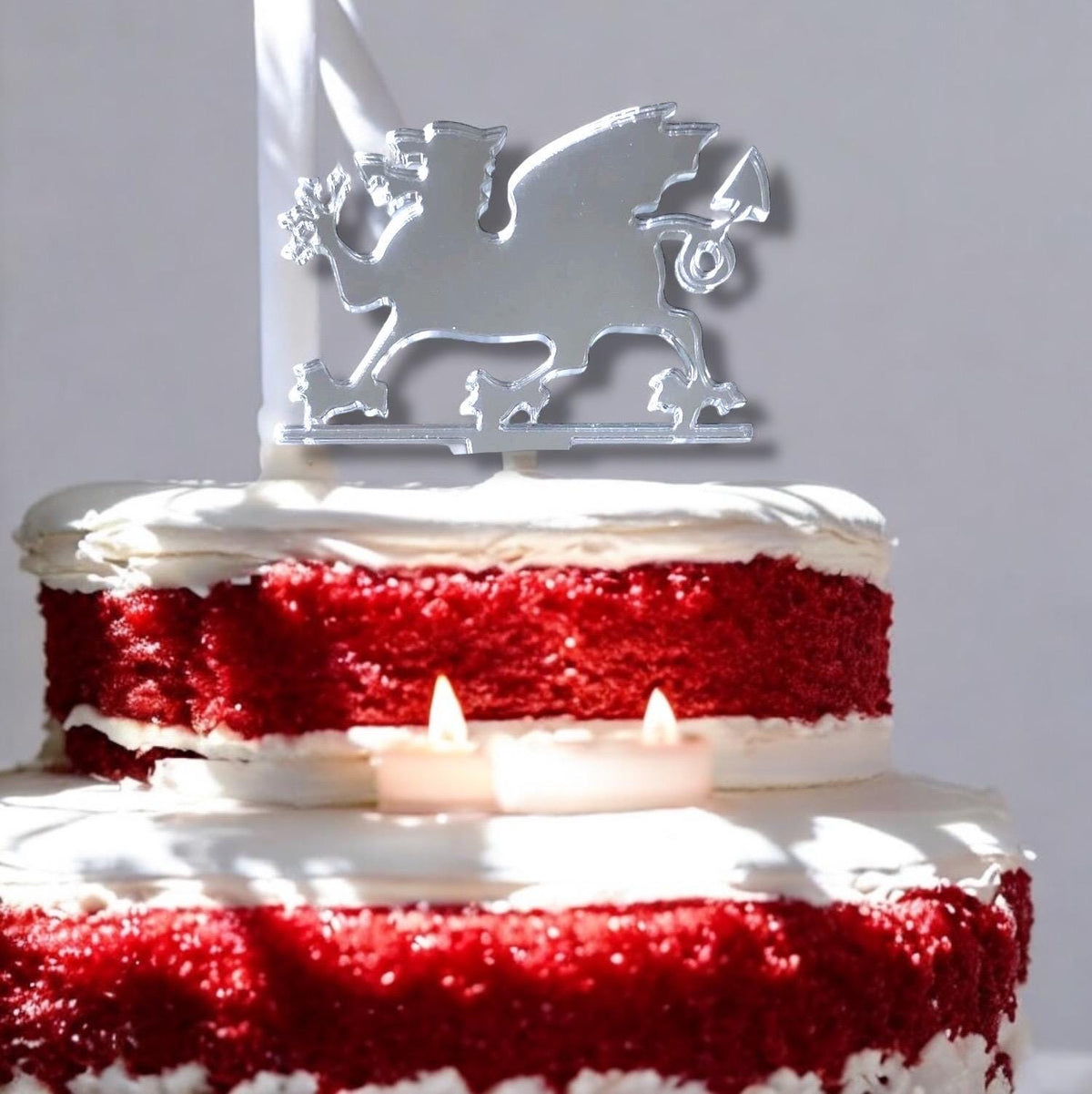 A mirrored, silver Welsh dragon silhouette cake topper placed on a tiered red velvet cake.