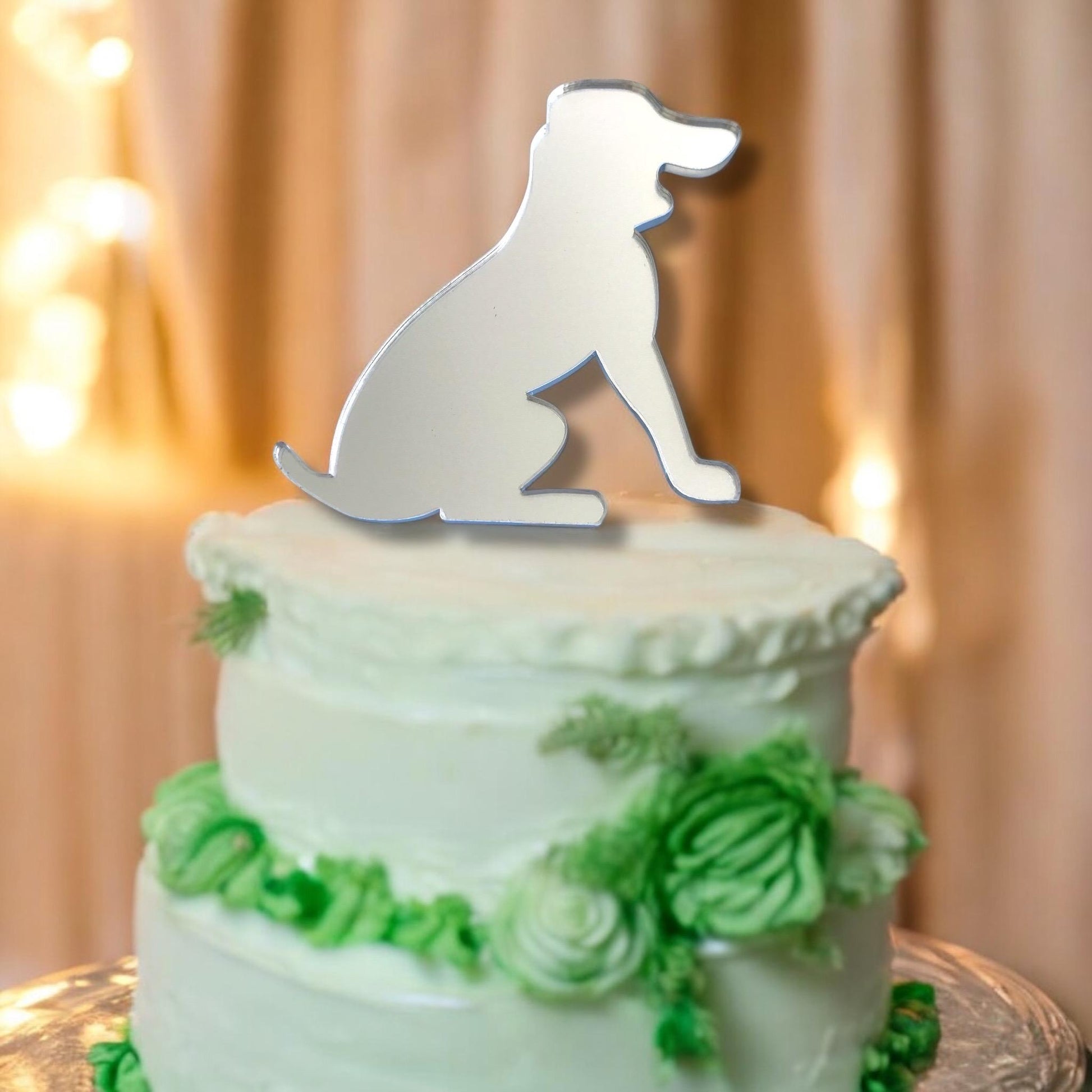 Silver mirrored acrylic beagle dog silhouette cake topper sitting on a two-tier white frosted cake with green florals.