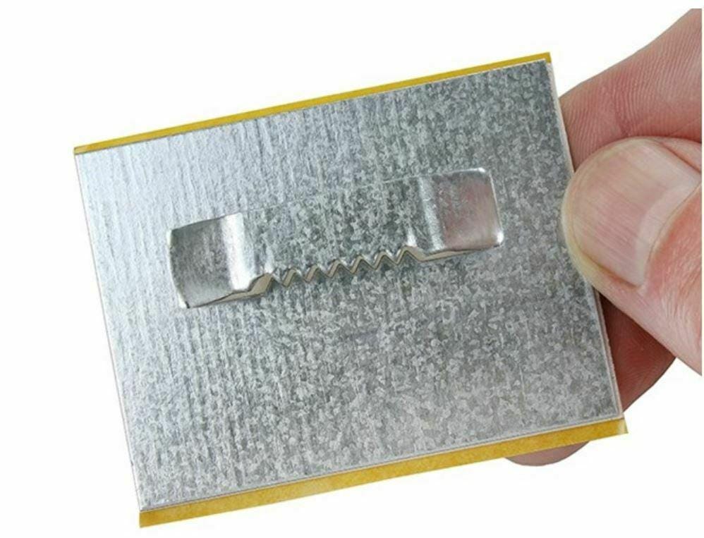 A hand holding a rectangular metal mirror hanging plate with a sawtooth hanger.