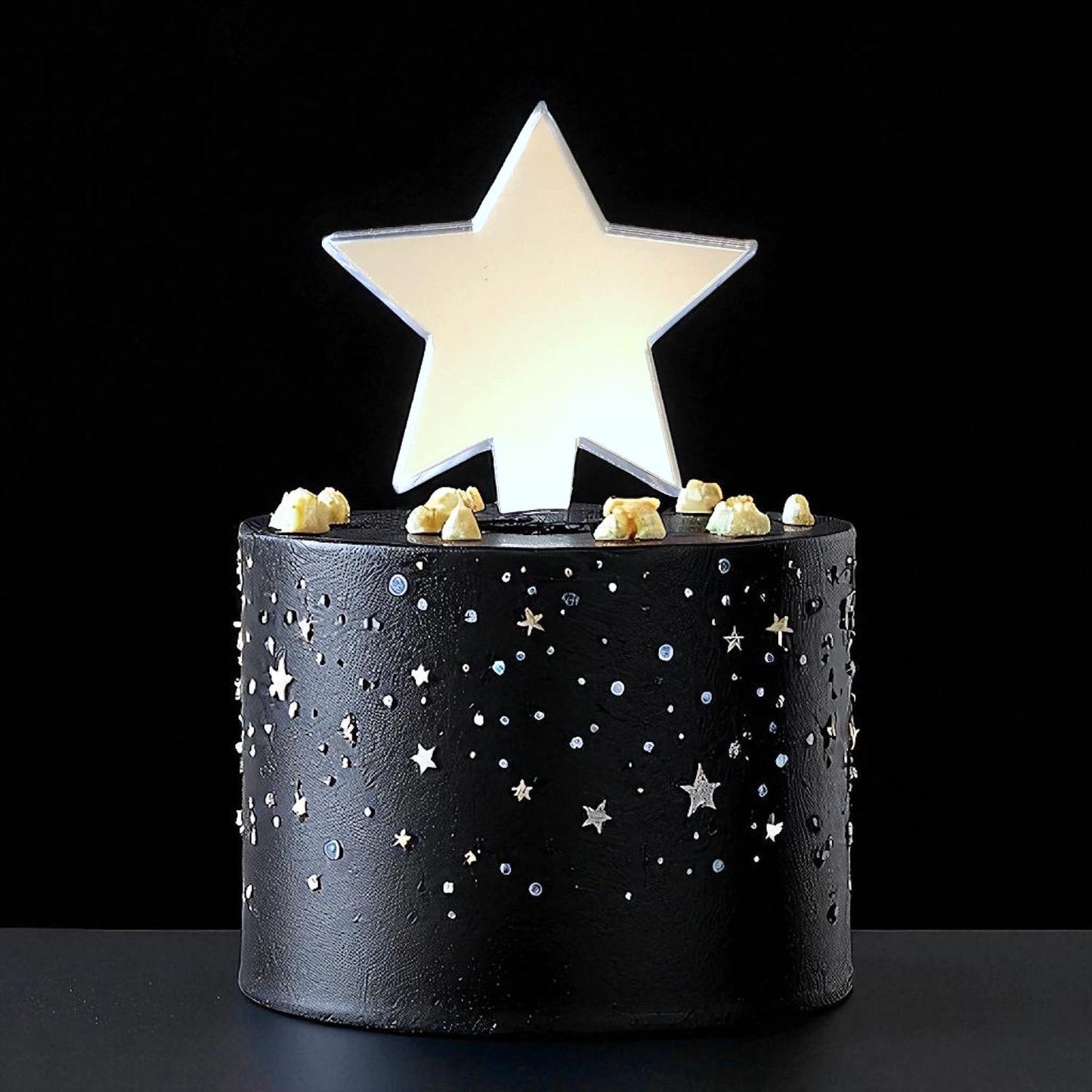 Shiny silver mirror-finish star cake topper centered on a black cake decorated with small silver star and dot accents.
