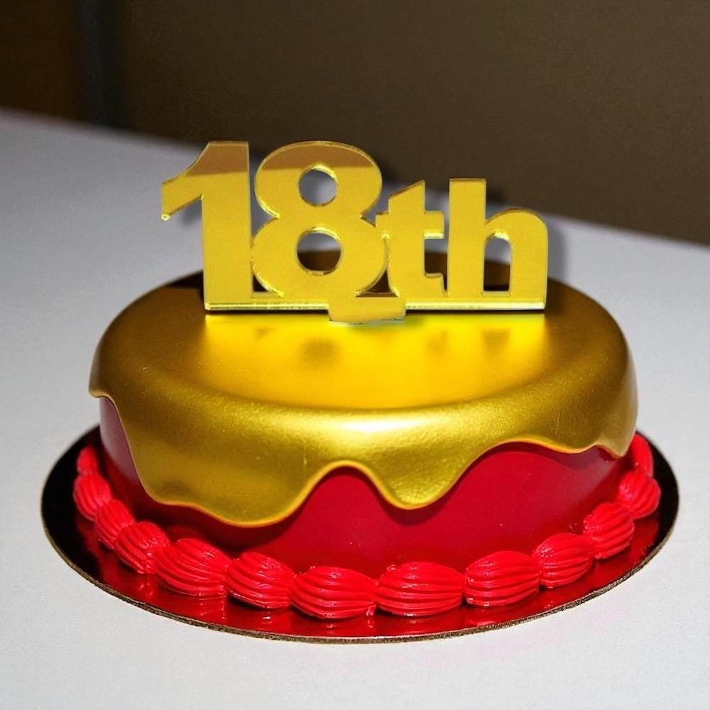 Shiny gold acrylic "18th" cake topper on a small red cake with gold icing drip and red piped border.