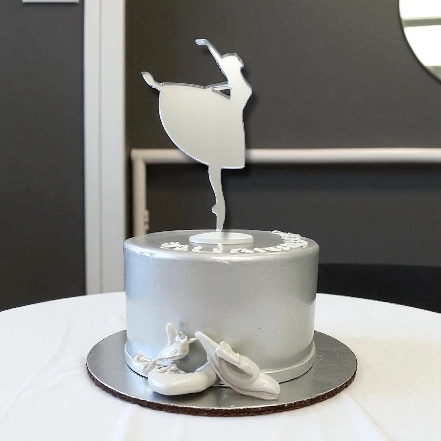 Mirrored silver acrylic ballerina silhouette cake topper standing on a silver frosted cake.