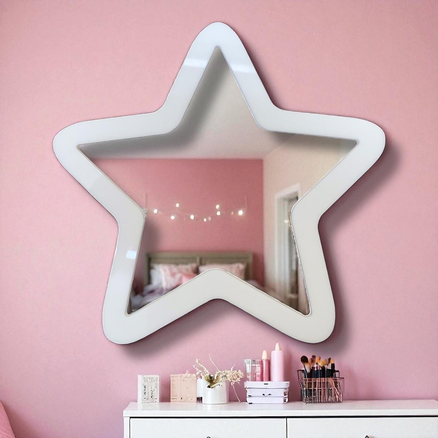 White star-shaped wall mirror hanging on a pink wall above a white dresser.
