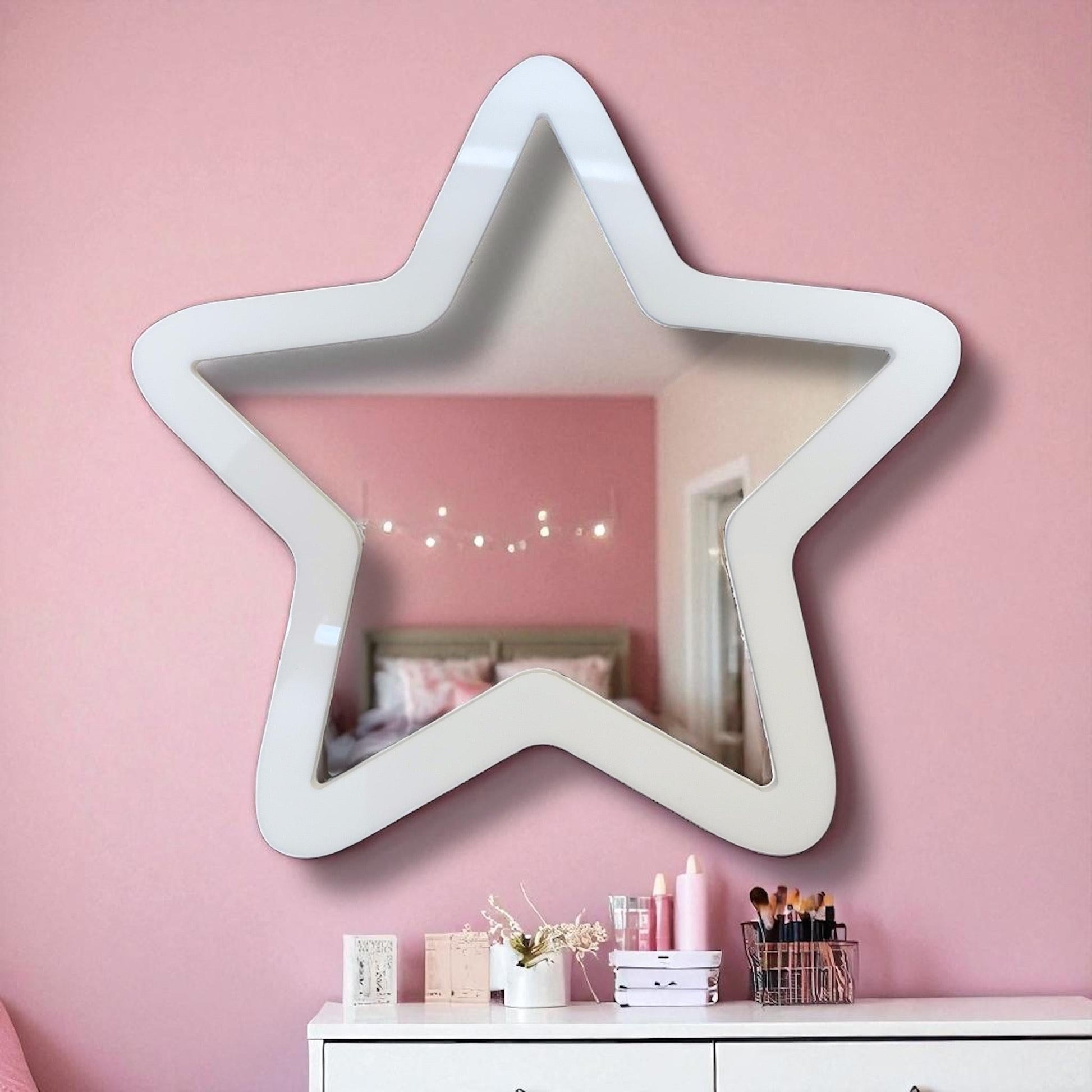 White star-shaped wall mirror hanging on a pink wall above a white dresser.