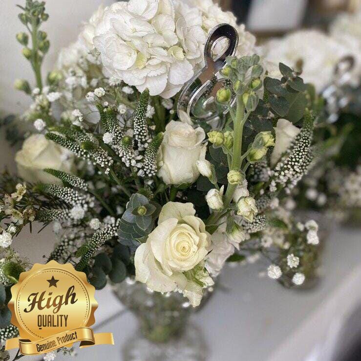 Shiny silver metallic musical note cake topper nestled in a white flower arrangement with a "High Quality" gold seal.