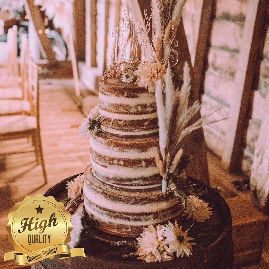 Clear acrylic "Mr & Mrs" cake topper with elegant script font, displayed on a tiered naked wedding cake.