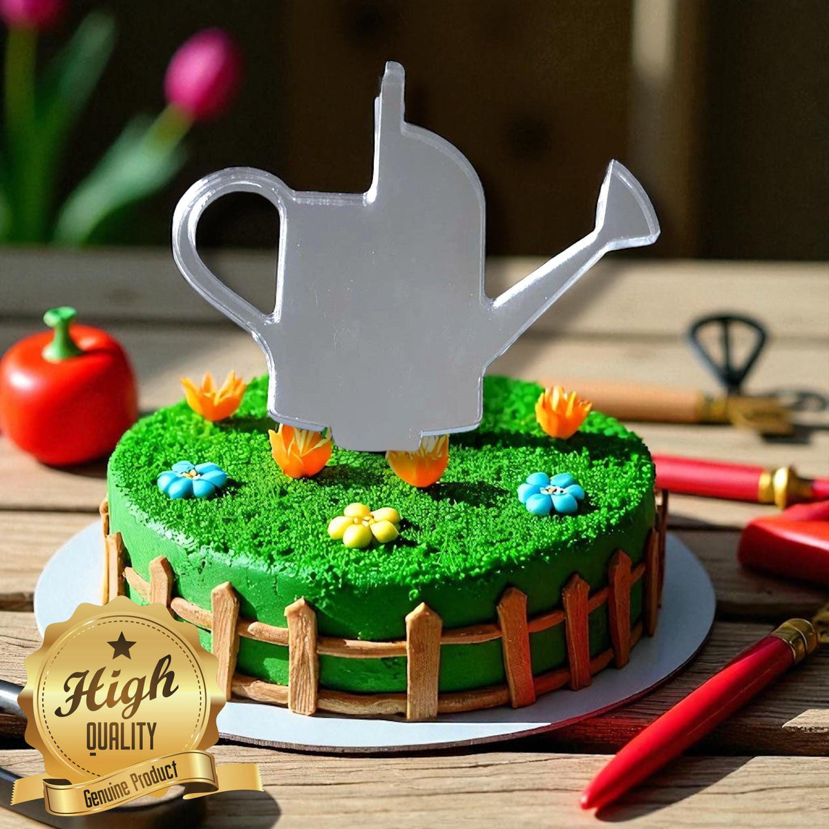 A reflective, silver watering can-shaped acrylic cake topper stands on a green, garden-themed cake with a picket fence.