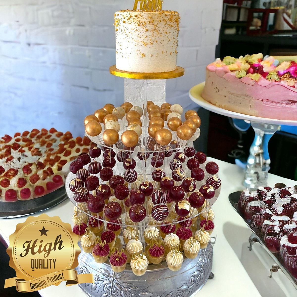 Multi-tiered clear acrylic cake pop and cake stand holding gold, maroon, and white desserts.