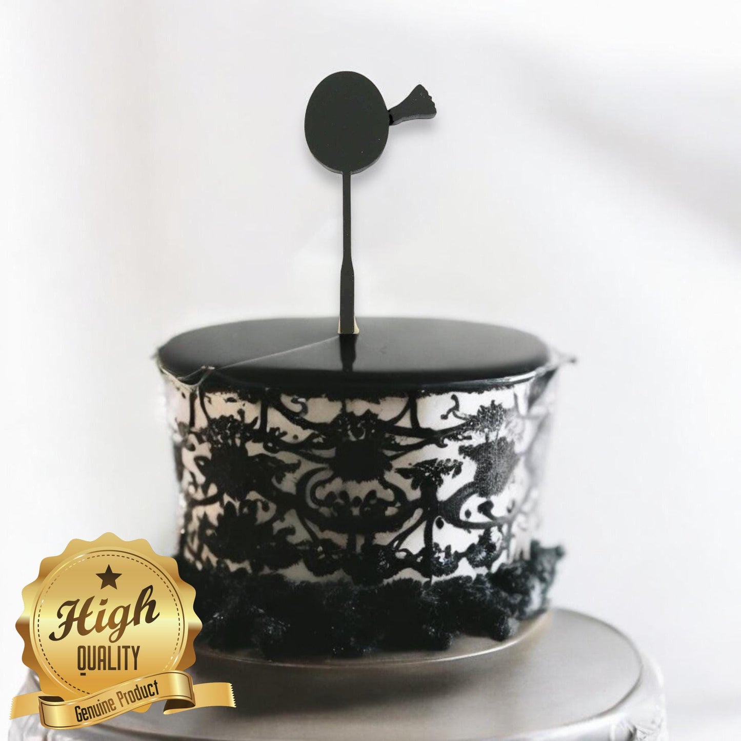 A black, minimalist badminton racket-shaped cake topper standing on a decorated cake with intricate black patterns.