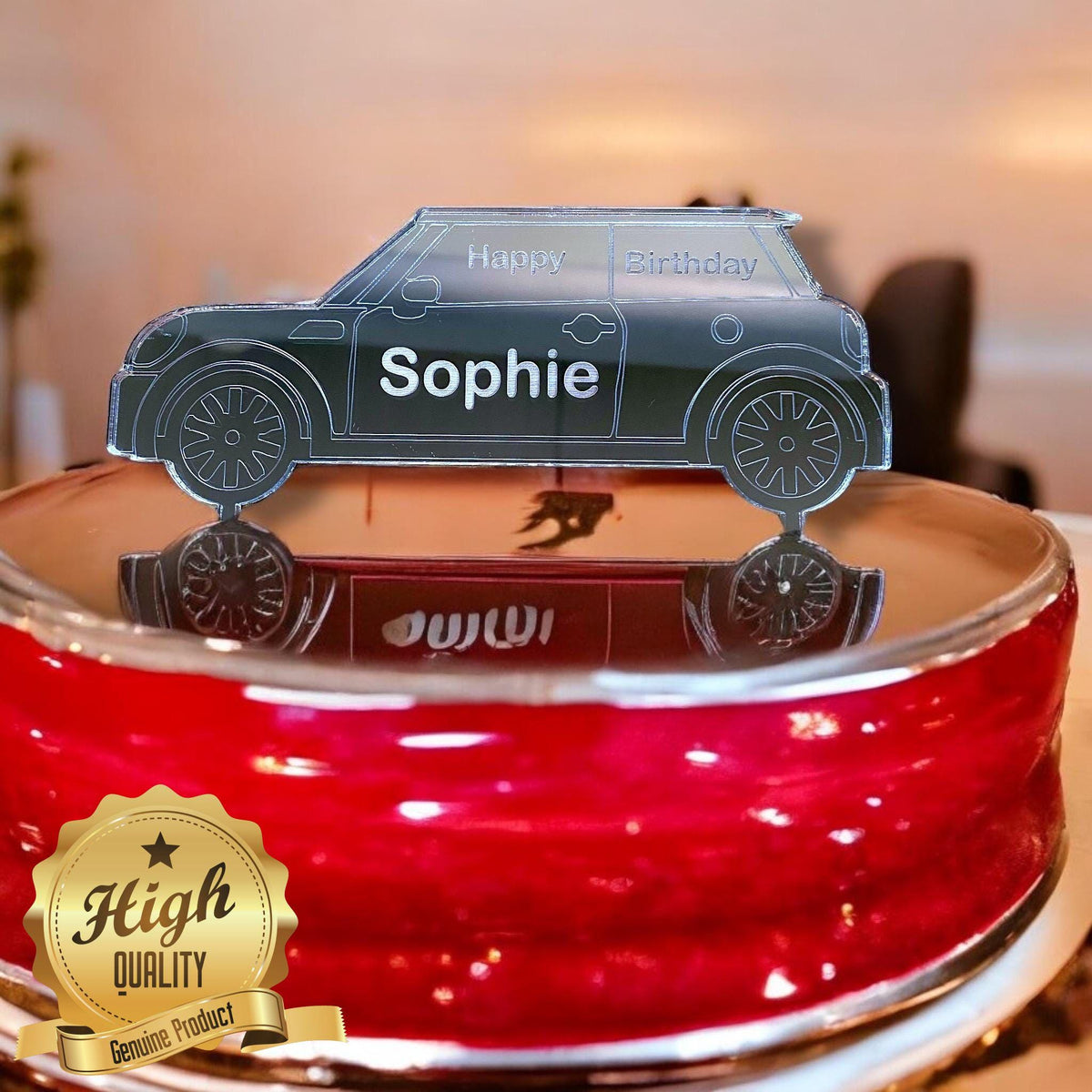 Black acrylic car-shaped cake topper engraved with "Happy Birthday" and the name "Sophie" on a red cake.