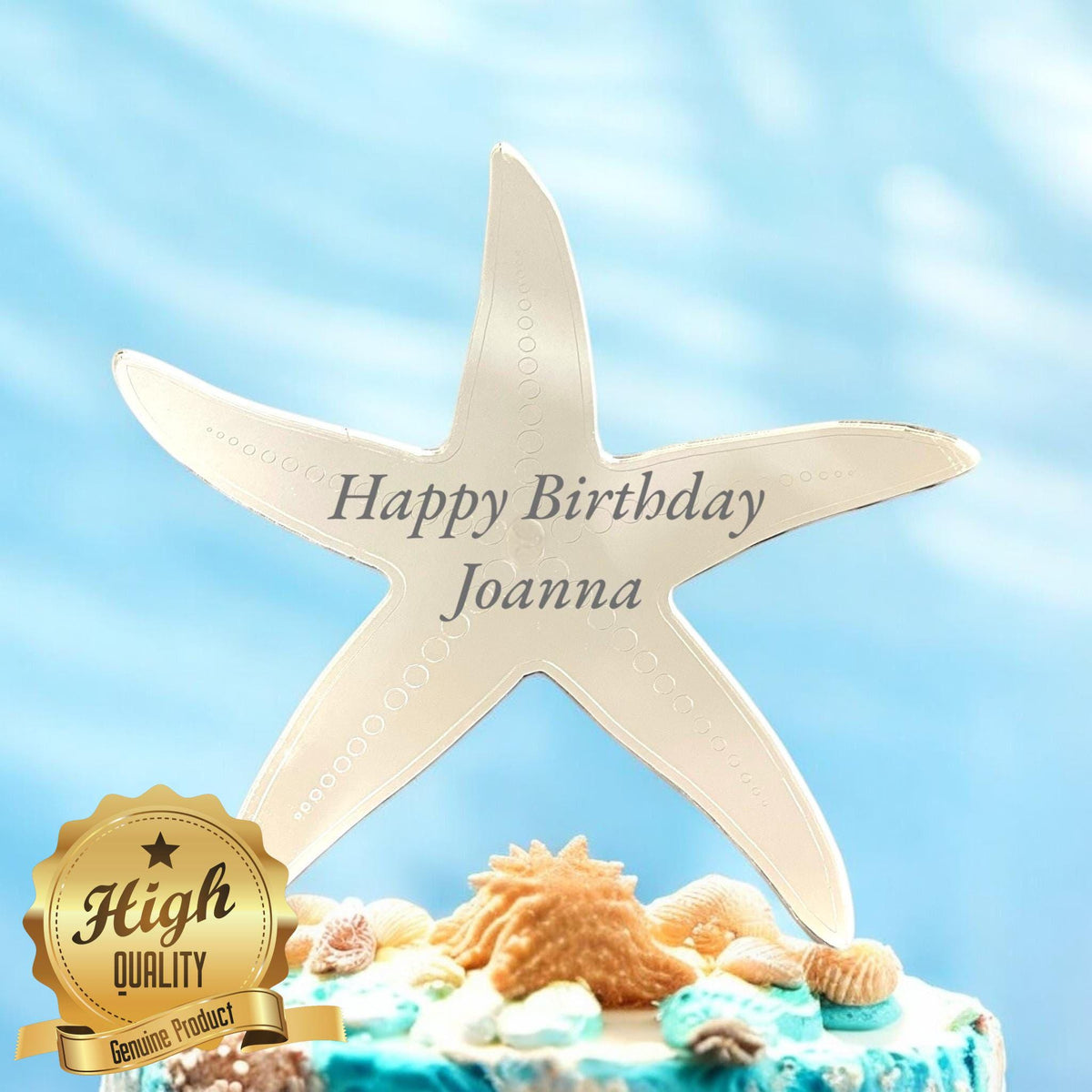 Gold mirrored acrylic starfish cake topper etched with "Happy Birthday Joanna" on a seashell-themed cake.