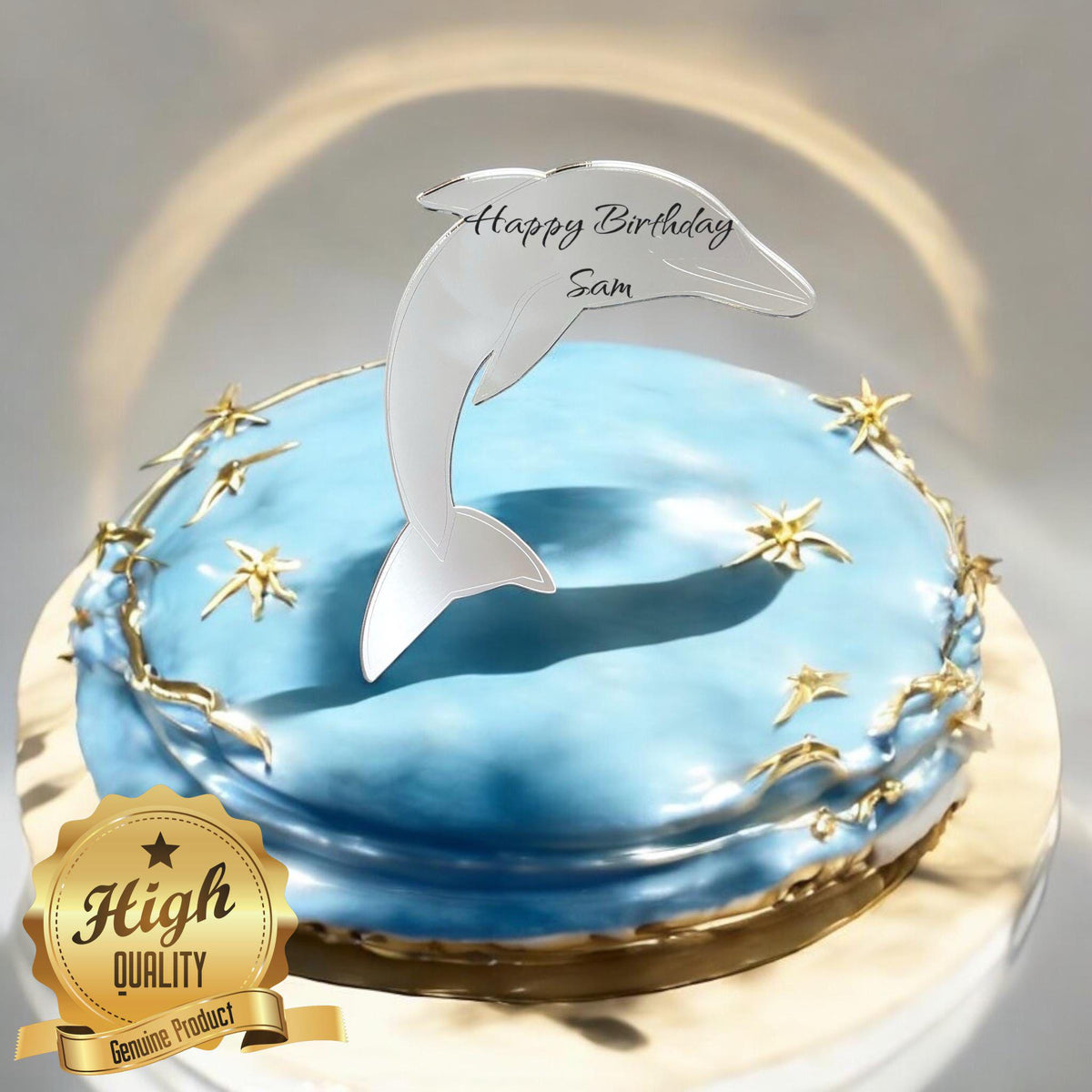 Silver mirrored acrylic dolphin cake topper etched with "Happy Birthday Sam" on a blue cake with gold stars.