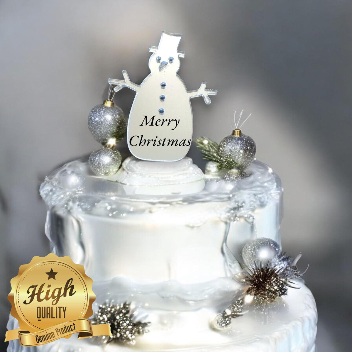 Silver mirrored snowman cake topper featuring a top hat and "Merry Christmas" text, placed on a white decorated cake.
