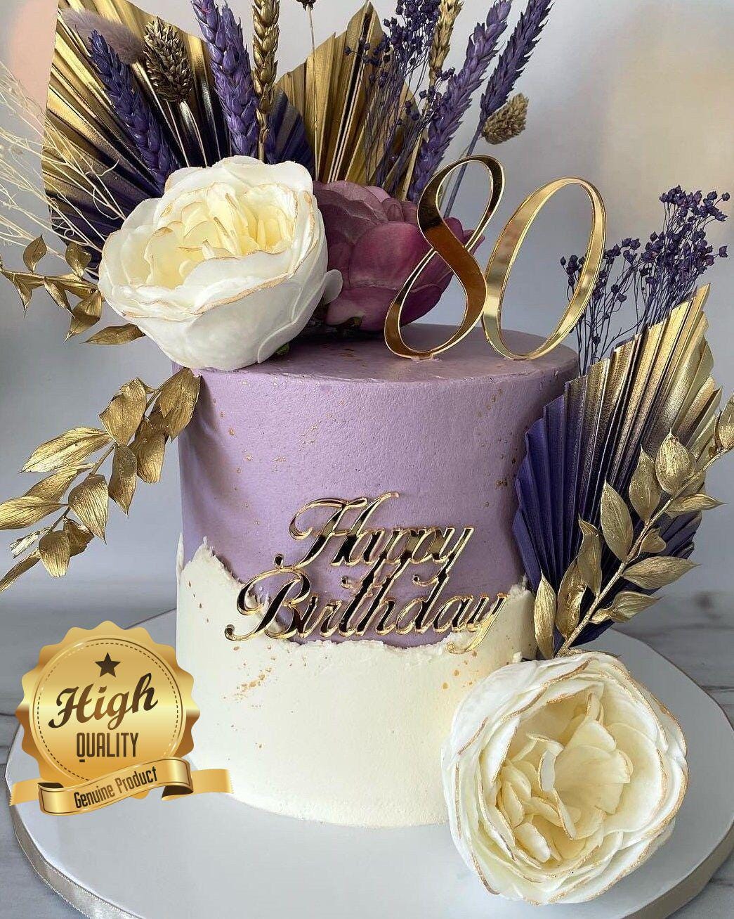 Gold mirror acrylic "80" and "Happy Birthday" cake toppers on a purple and cream frosted cake with floral decor.