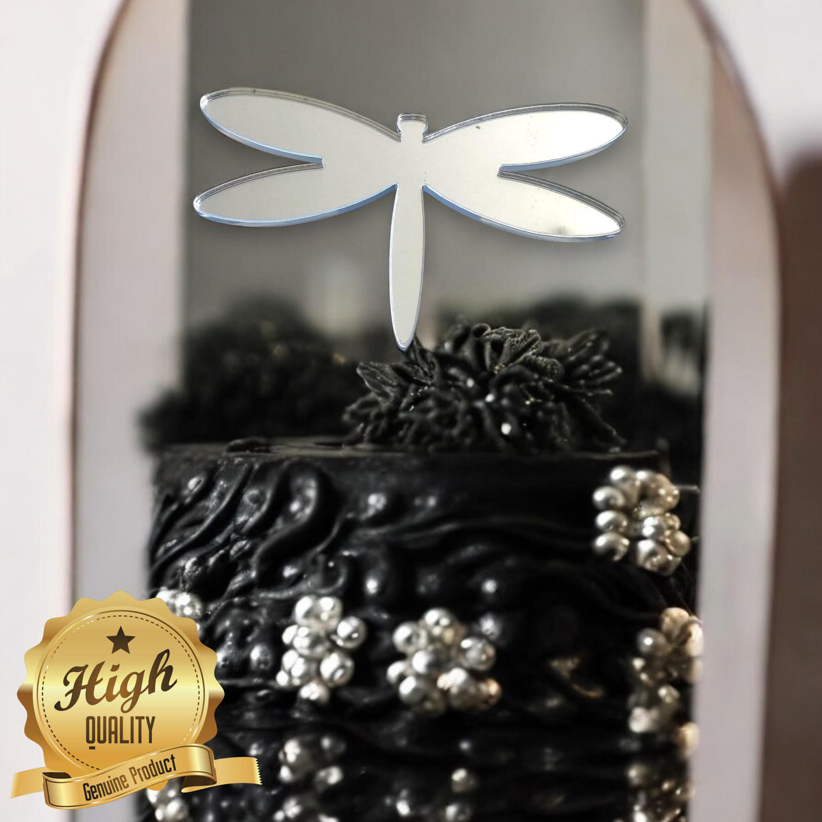 A mirrored silver dragonfly cake topper resting on a textured black cupcake with silver accents.