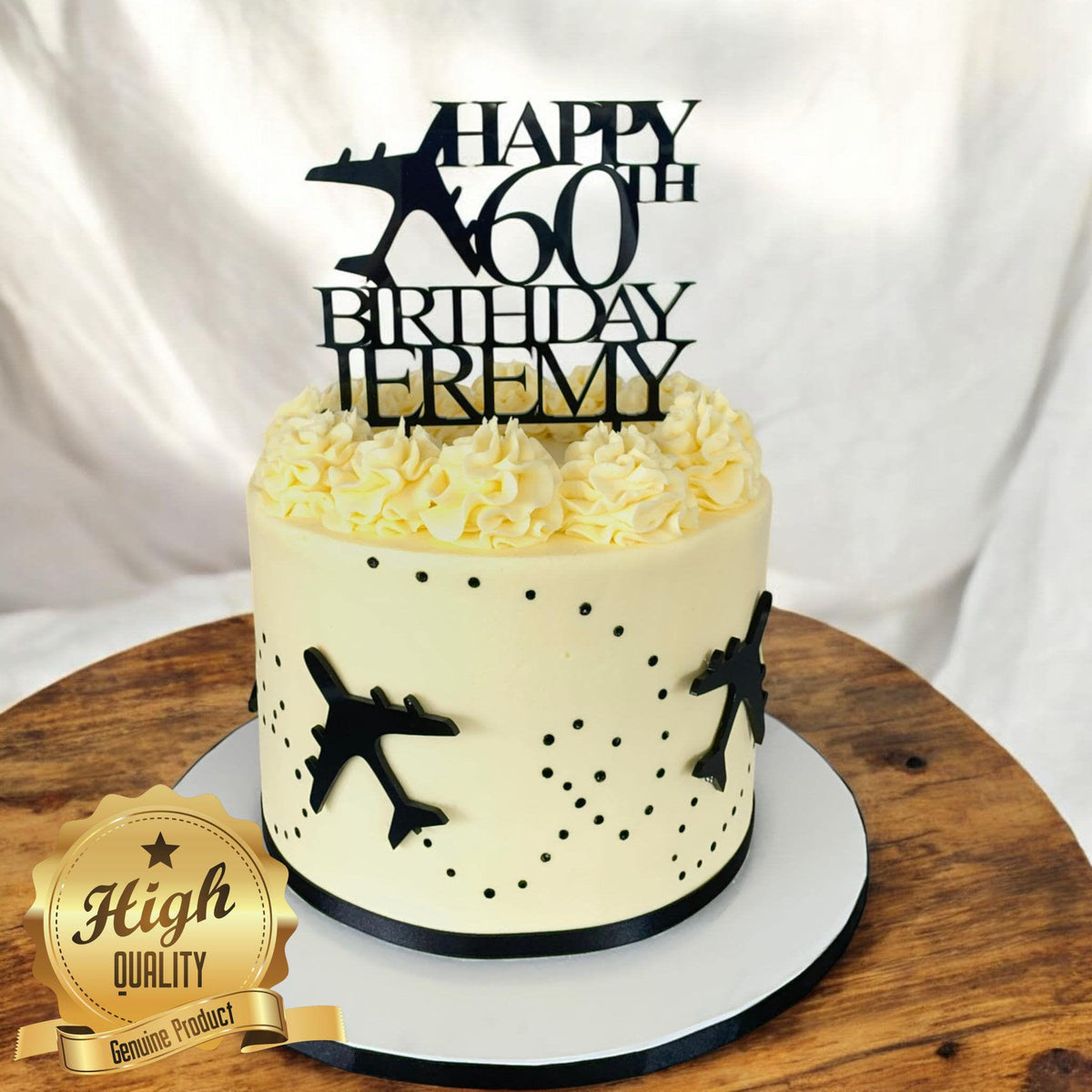 Black acrylic cake topper reading "Happy 60th Birthday Jeremy" with an airplane silhouette on a white frosted cake.