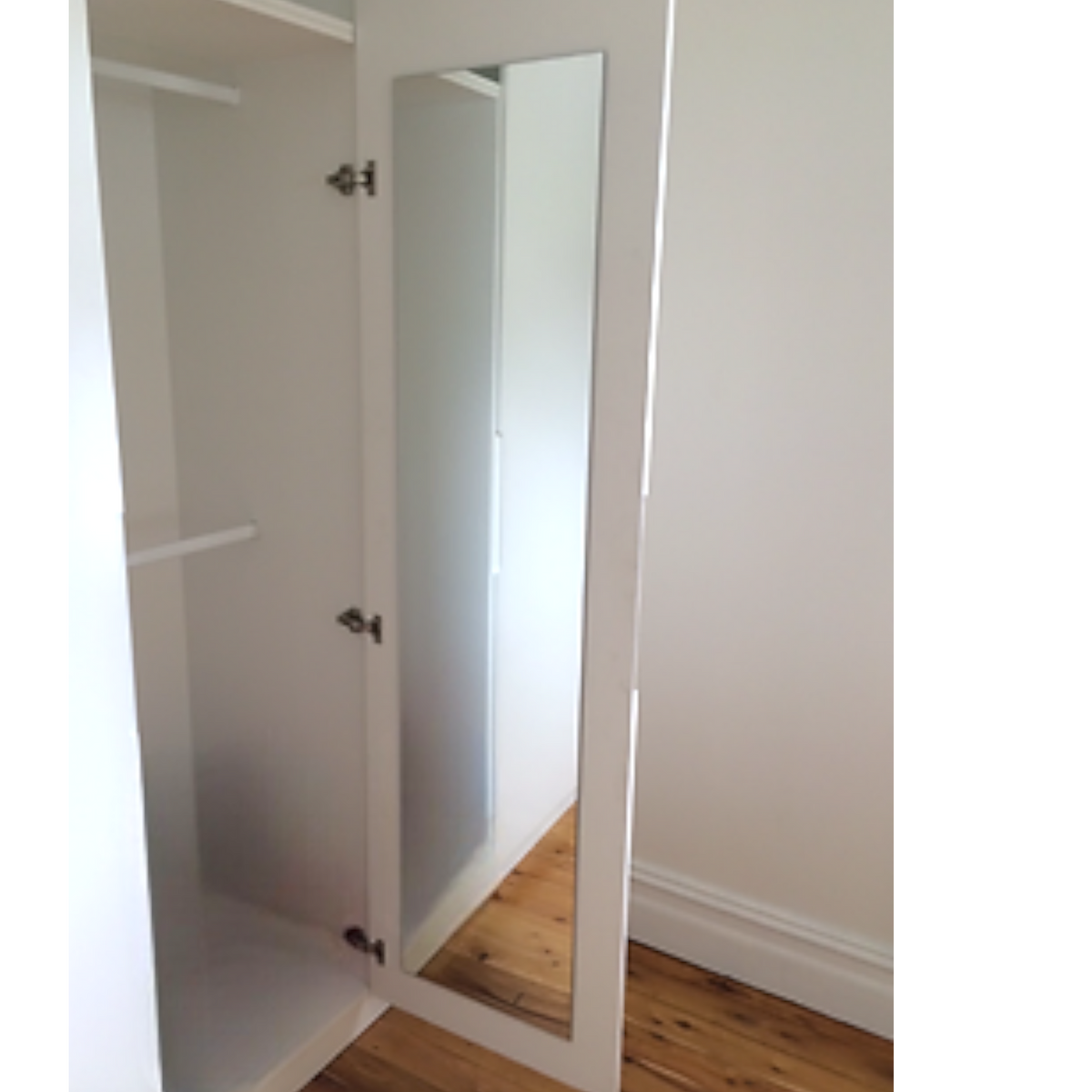 Rectangular glass mirror mounted on the inside of a white wardrobe door.