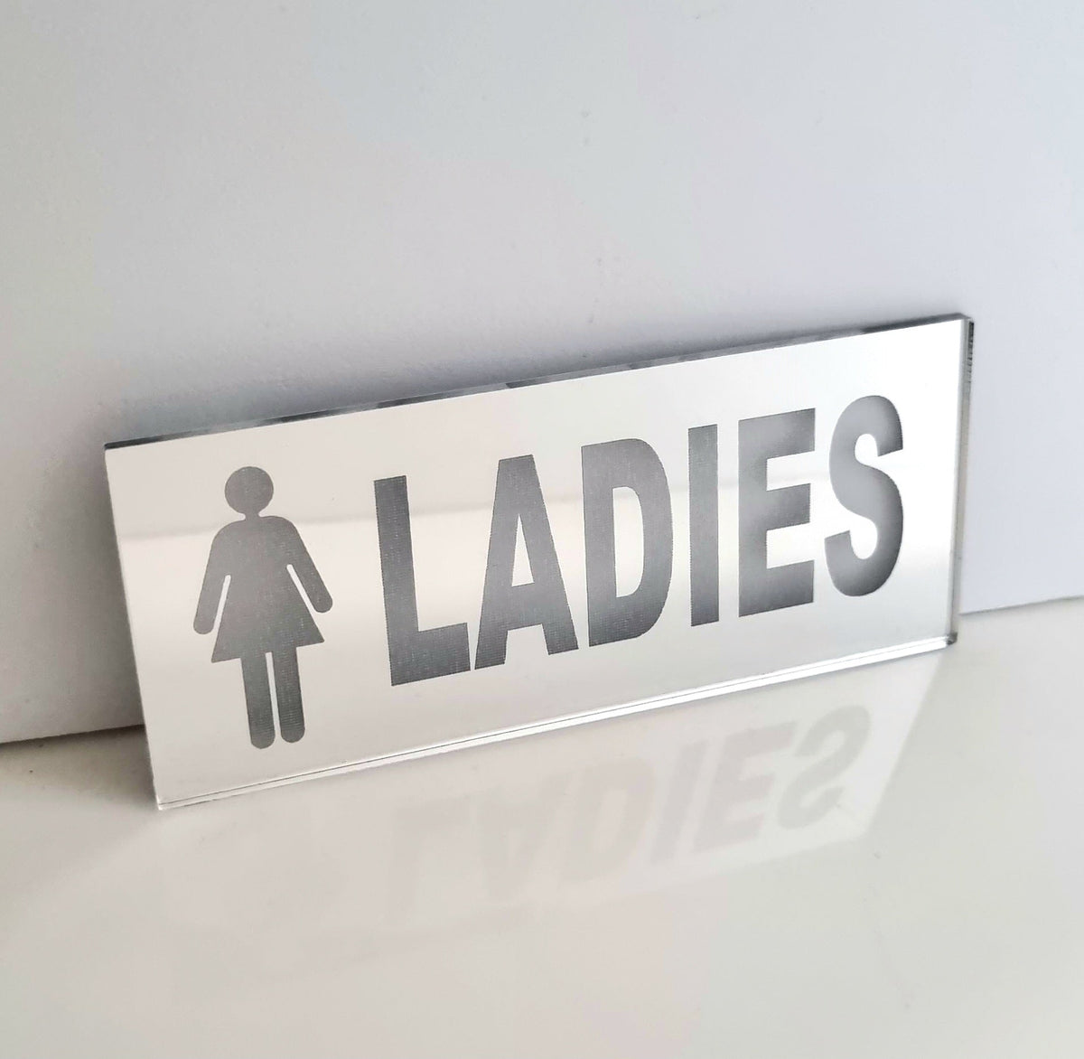 Rectangular mirrored acrylic ladies toilet sign with a female symbol and the word LADIES.