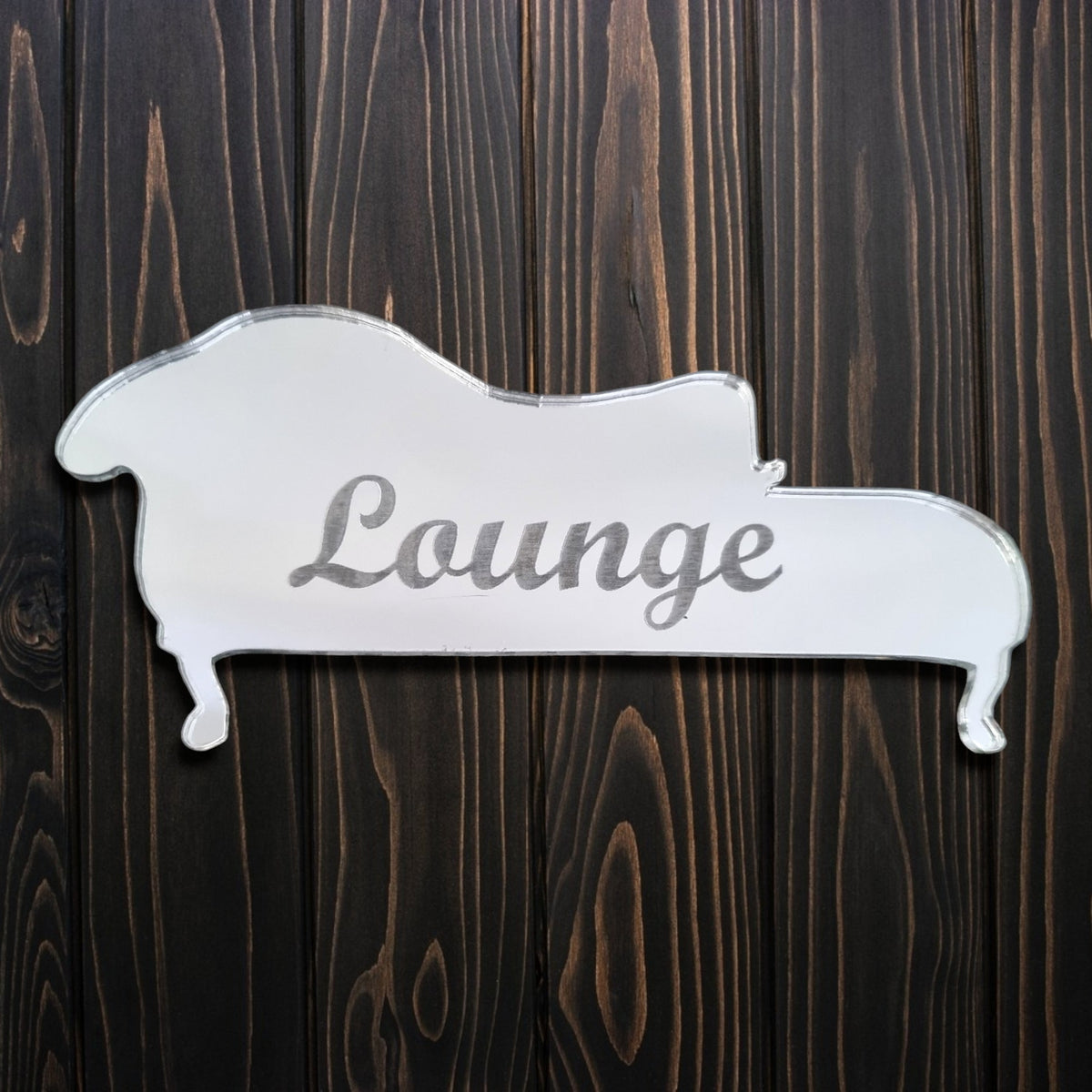 Chai-shaped silver mirror engraved with the word "Lounge" in cursive, on a dark wood background.