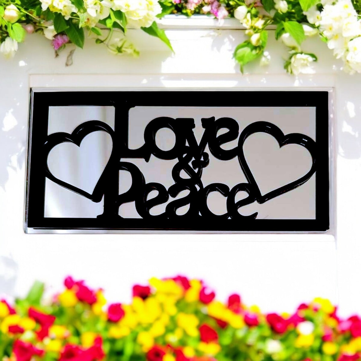 Rectangular black garden mirror with "Love & Peace" text and heart cutouts, mounted on a white wall.