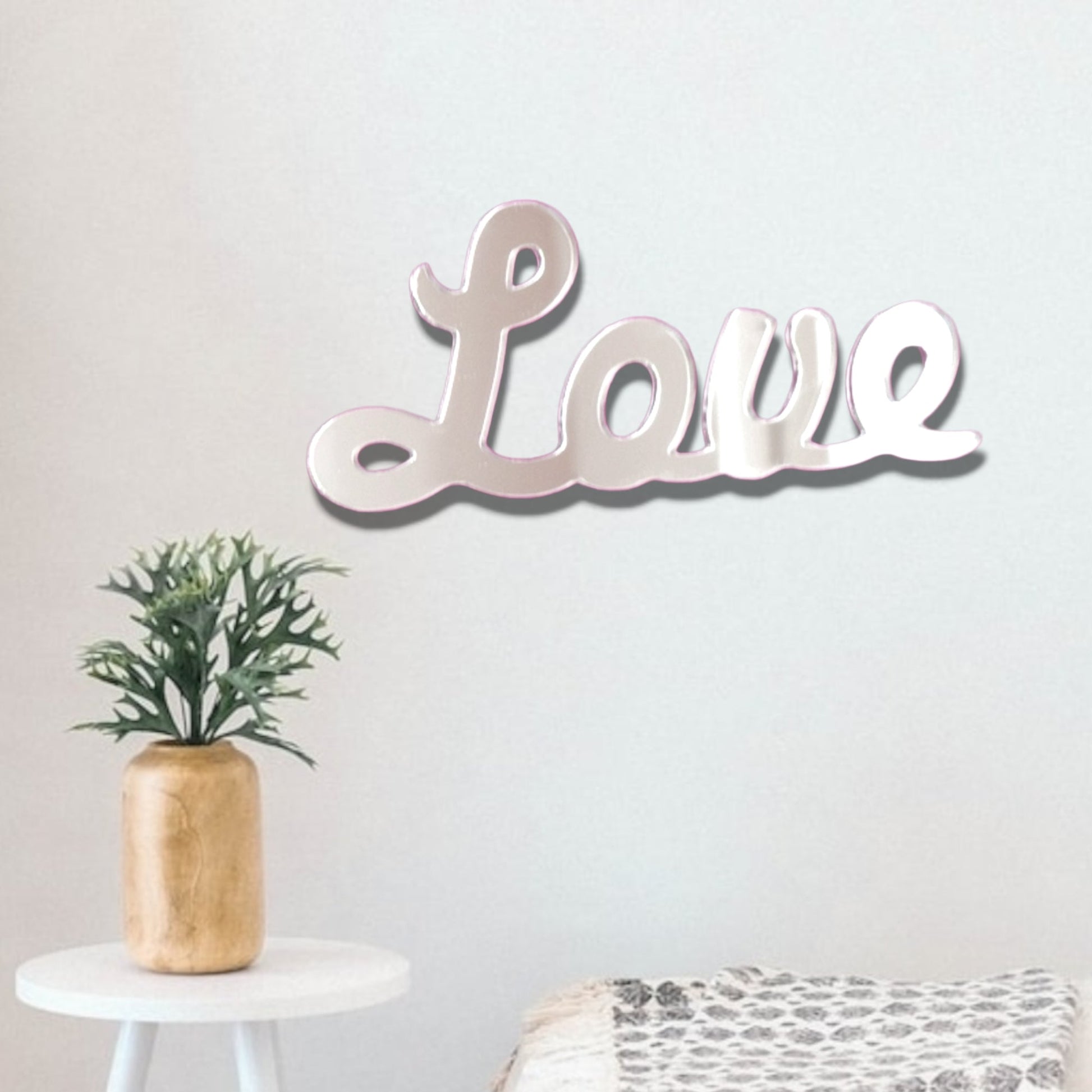 A "Love" script mirror hung on a white wall above a small table with a potted plant.
