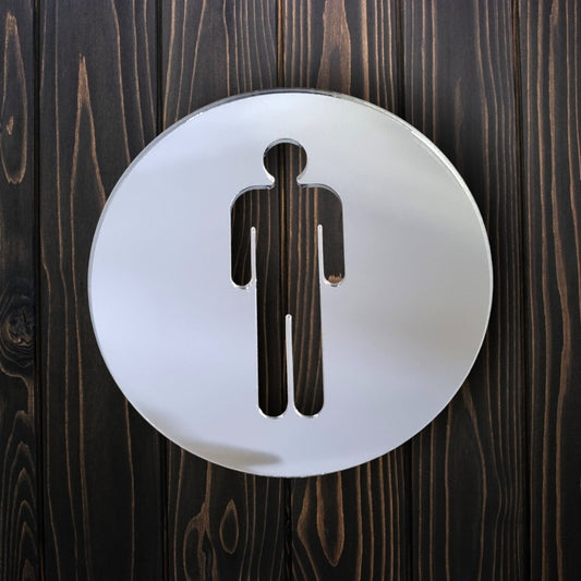 Round mirrored male toilet sign mounted on dark vertical wooden planks.