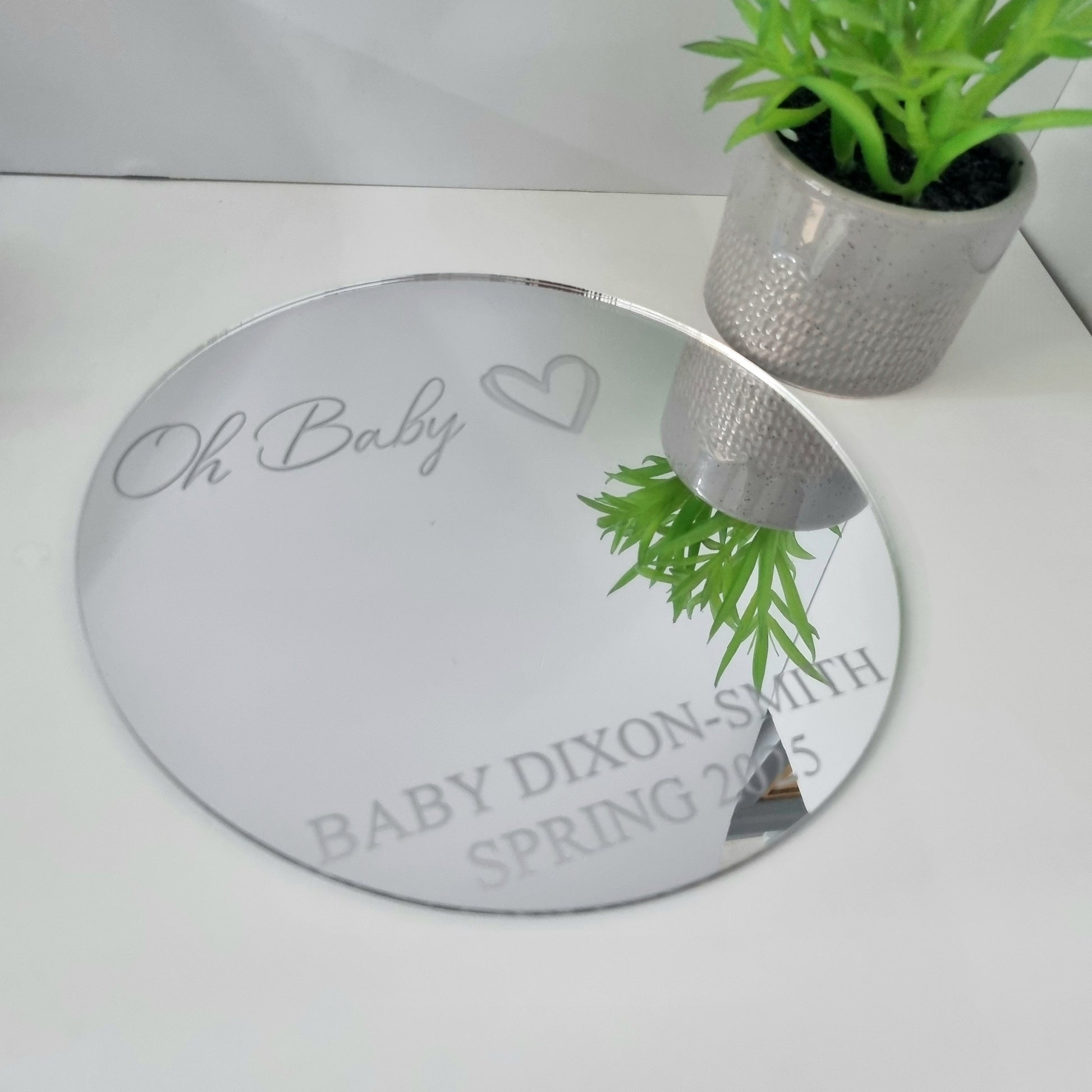Personalised round mirror engraved with "Oh Baby," a heart, and custom text "BABY DIXON-SMITH SPRING 2025."