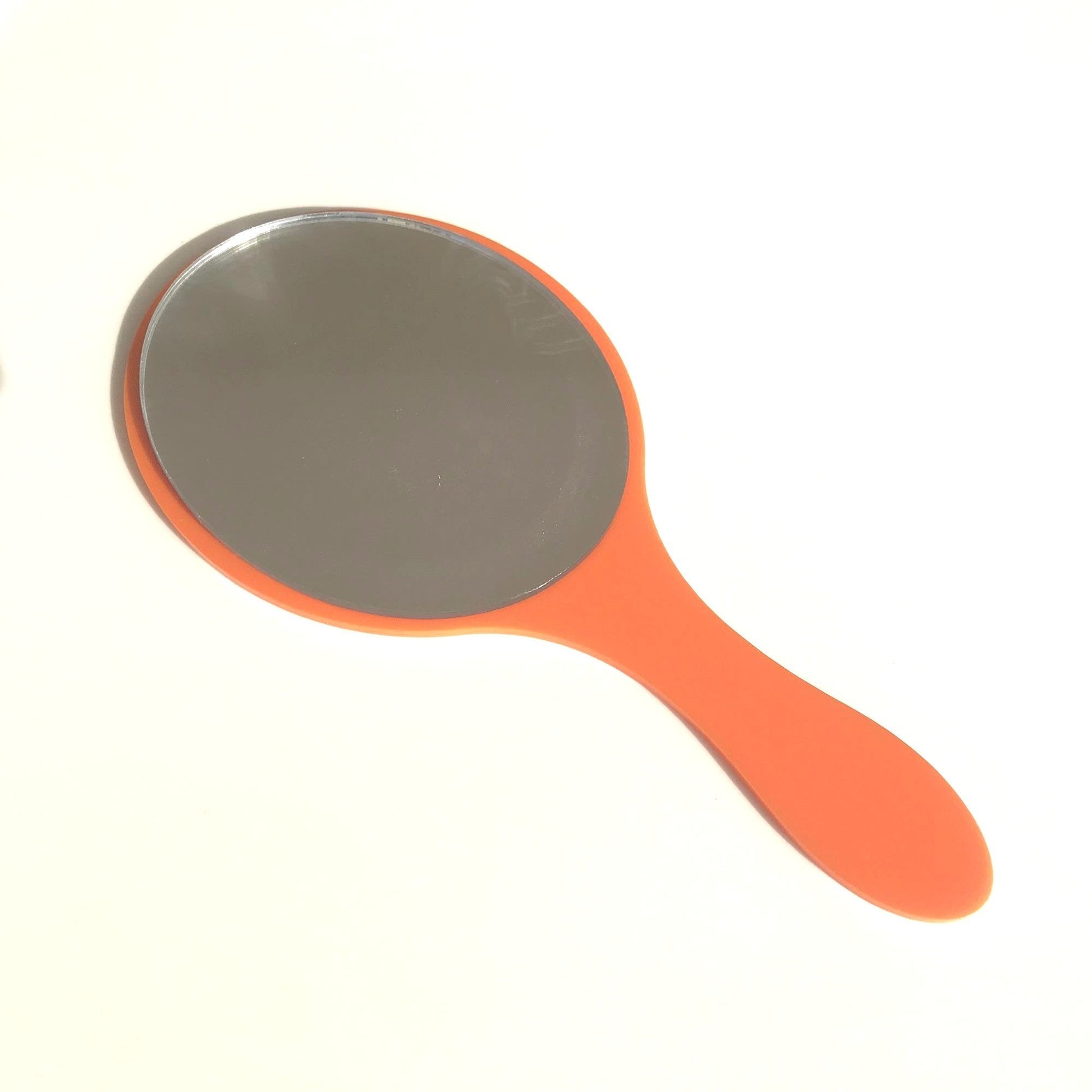An oval hand-held mirror with a glossy orange handle on a white background.