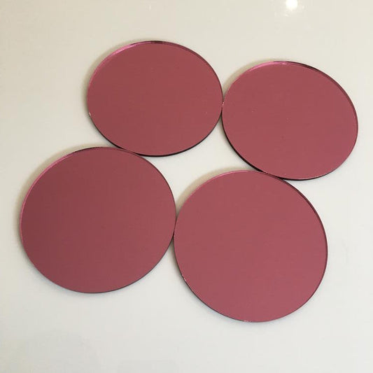 Four round pink mirror tiles arranged on a white surface.