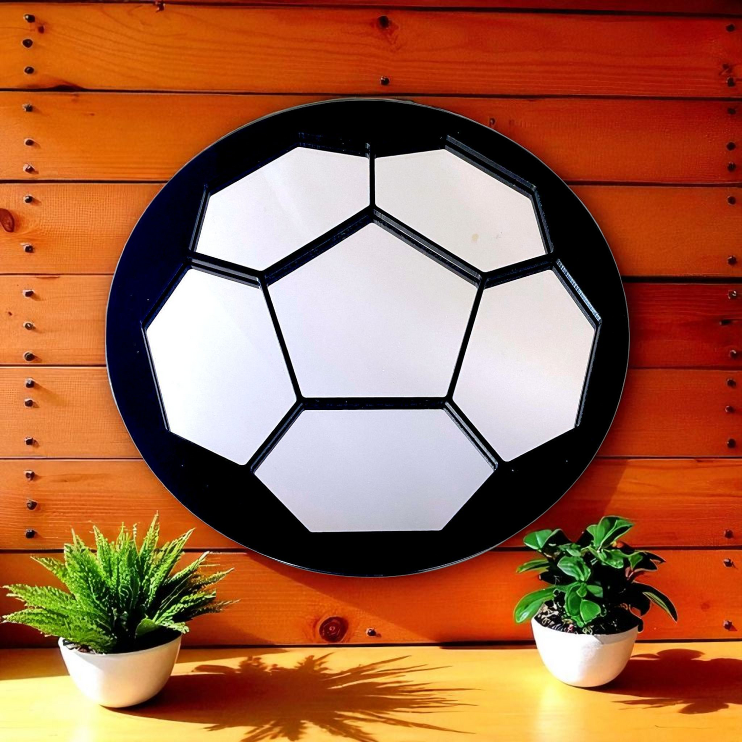 Round football-patterned mirror with segmented mirror panels and a black frame, hung on a wood wall.