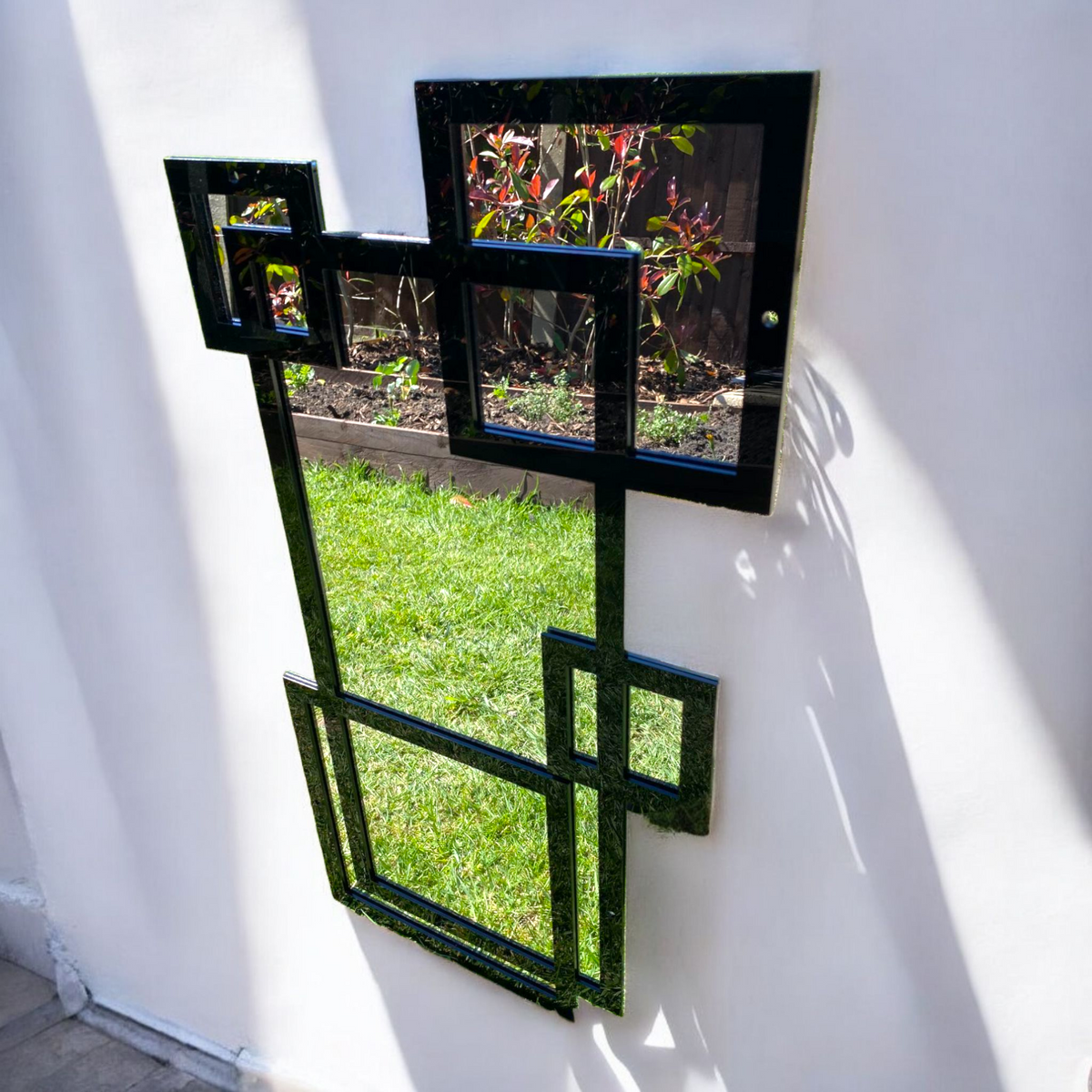 Contemporary black square garden mirror hanging on a white outdoor wall.