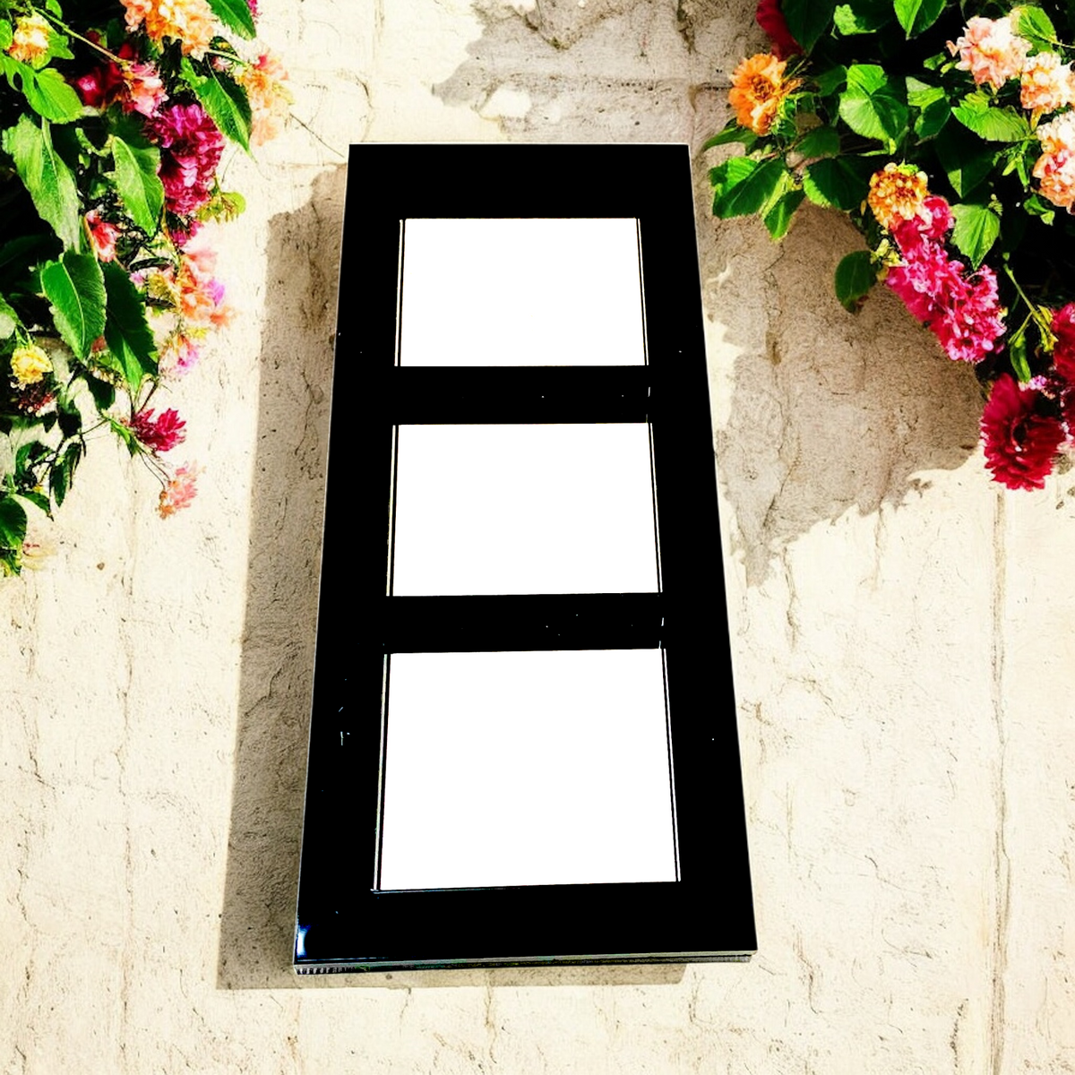 Black rectangular three-panel garden mirror mounted on a stone wall between flowers.