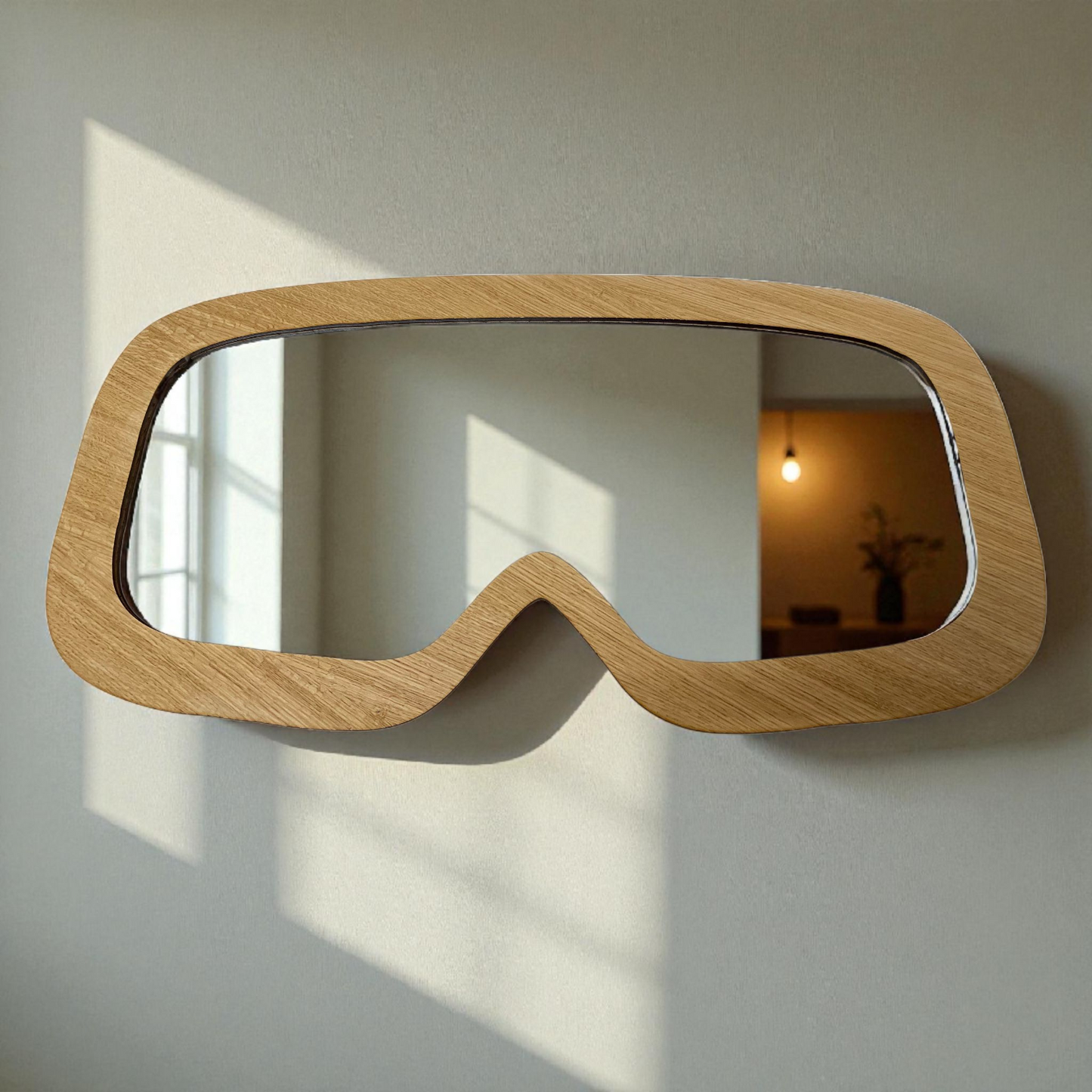 Ski goggle-shaped wall mirror with a light wood frame hanging on a plain gray wall.