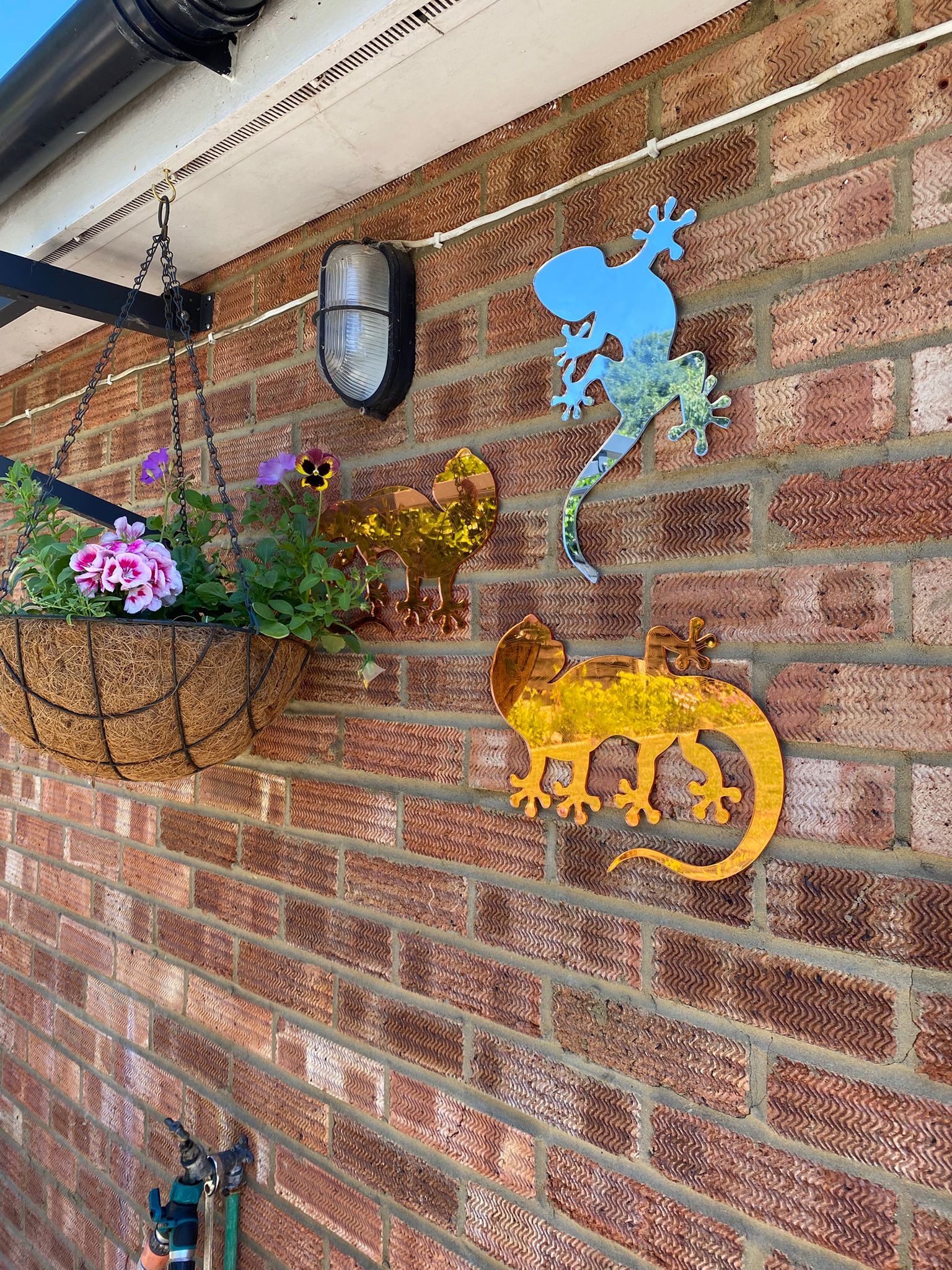 Three gecko-shaped mirrors mounted on an exterior red brick wall, featuring blue and gold tints.