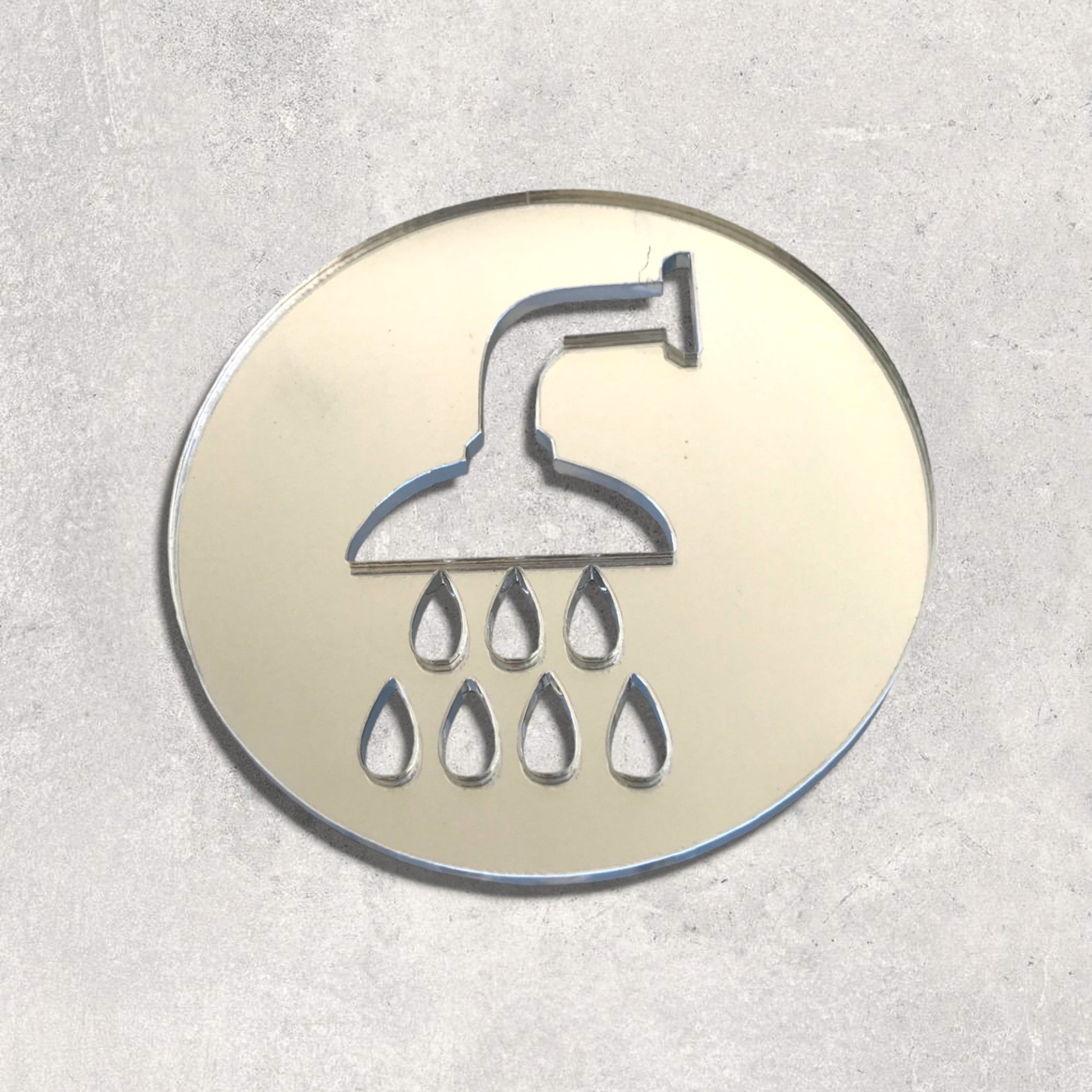 A round mirrored shower room sign with an engraved showerhead and water drops on a gray background.