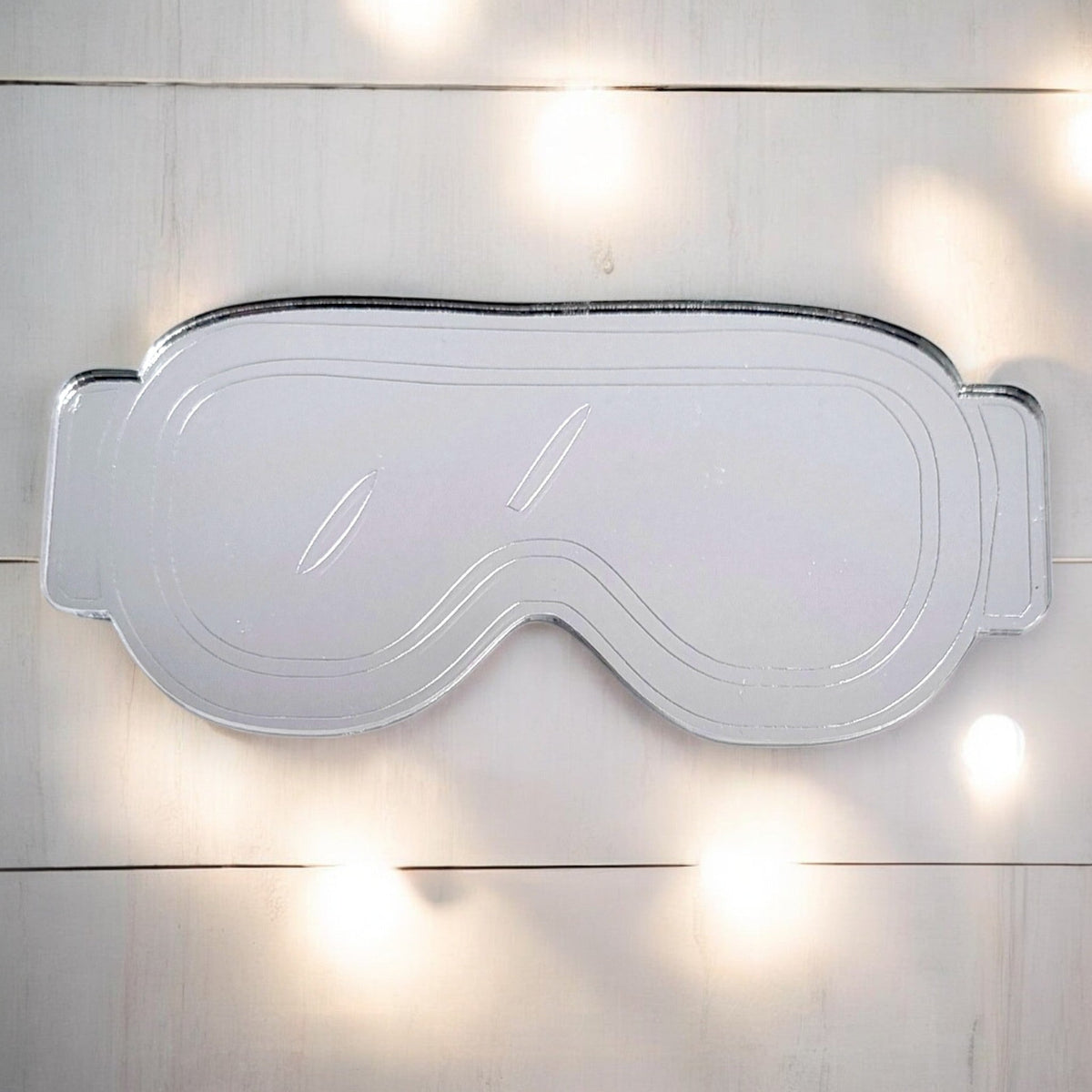 Silver ski goggles-shaped mirror on a white wooden surface.