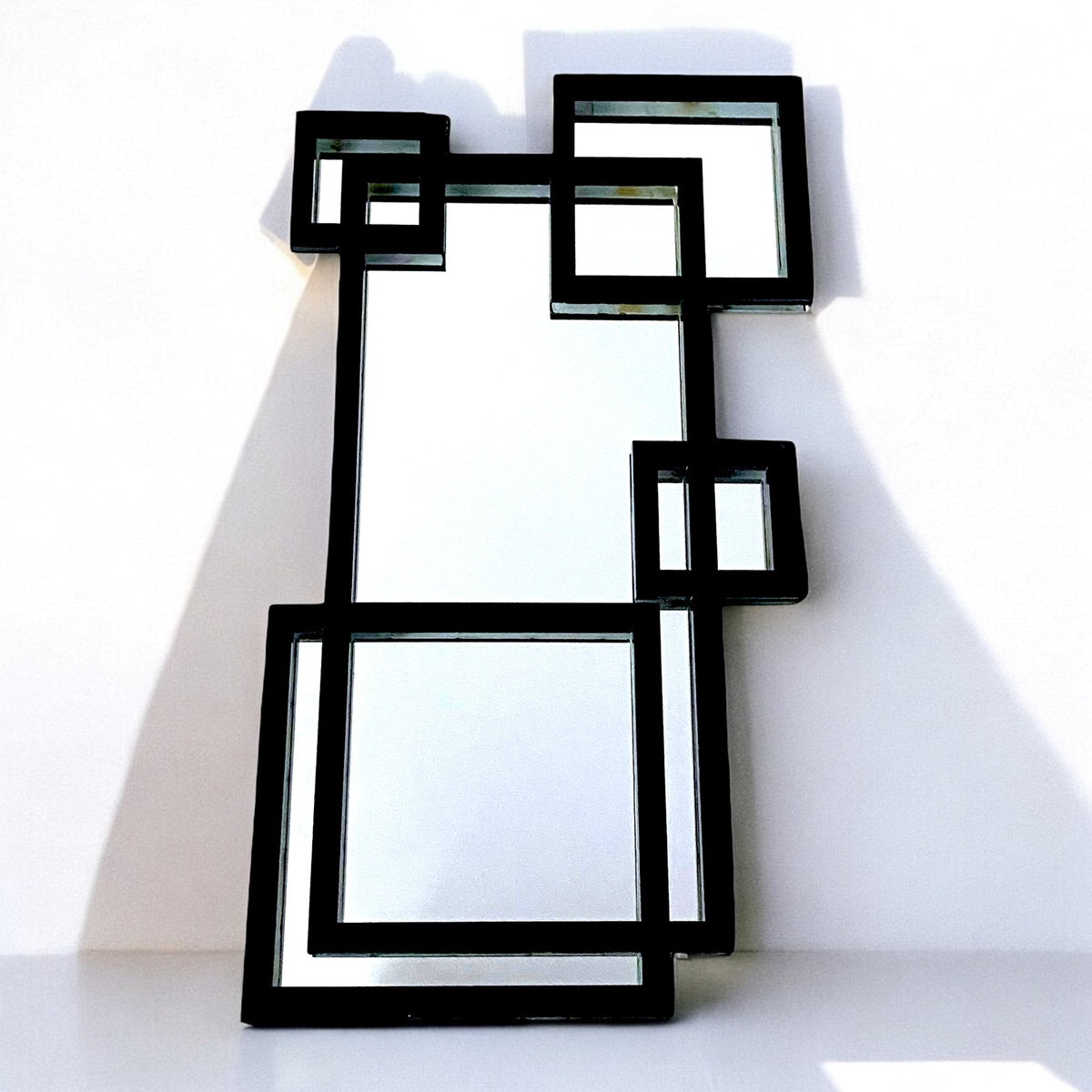 Contemporary black-framed garden mirror with an overlapping squares and rectangles geometric design against a white wall.