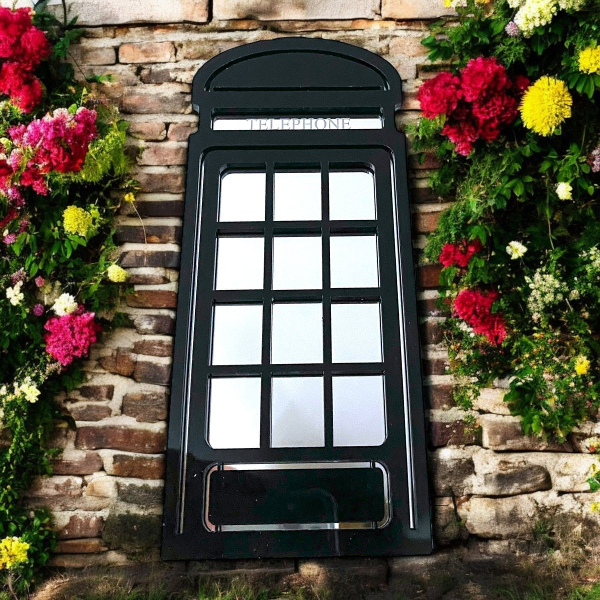 Black wooden arched telephone box garden mirror hanging on a stone wall between flowers.