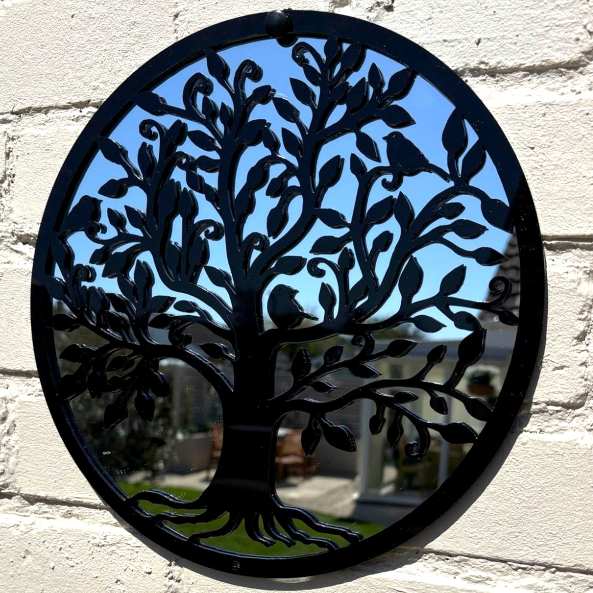 Round black metal garden mirror featuring an intricate Tree of Life cut-out design.