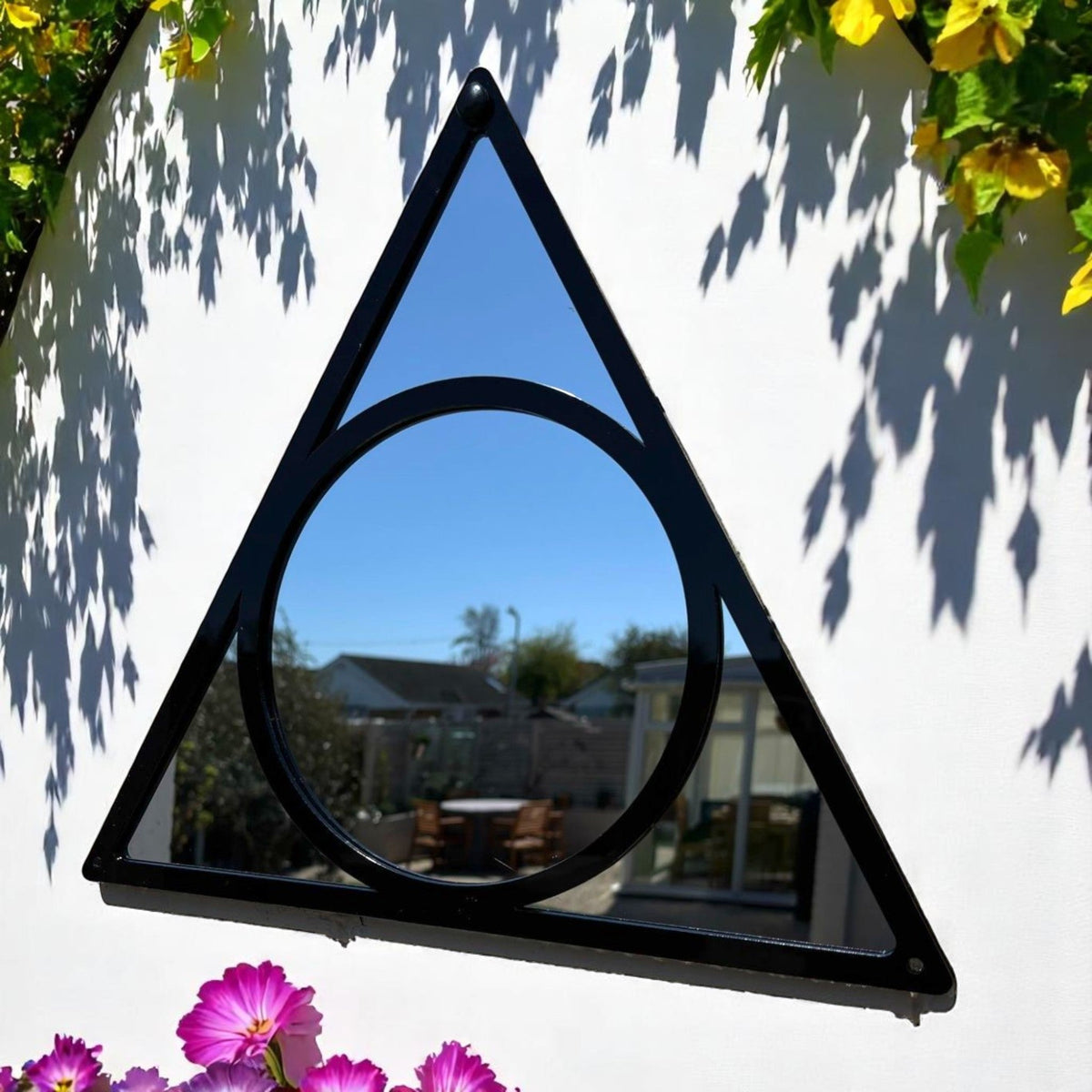 Triangle and circle garden mirror with a black metal frame, mounted on a white wall outdoors.