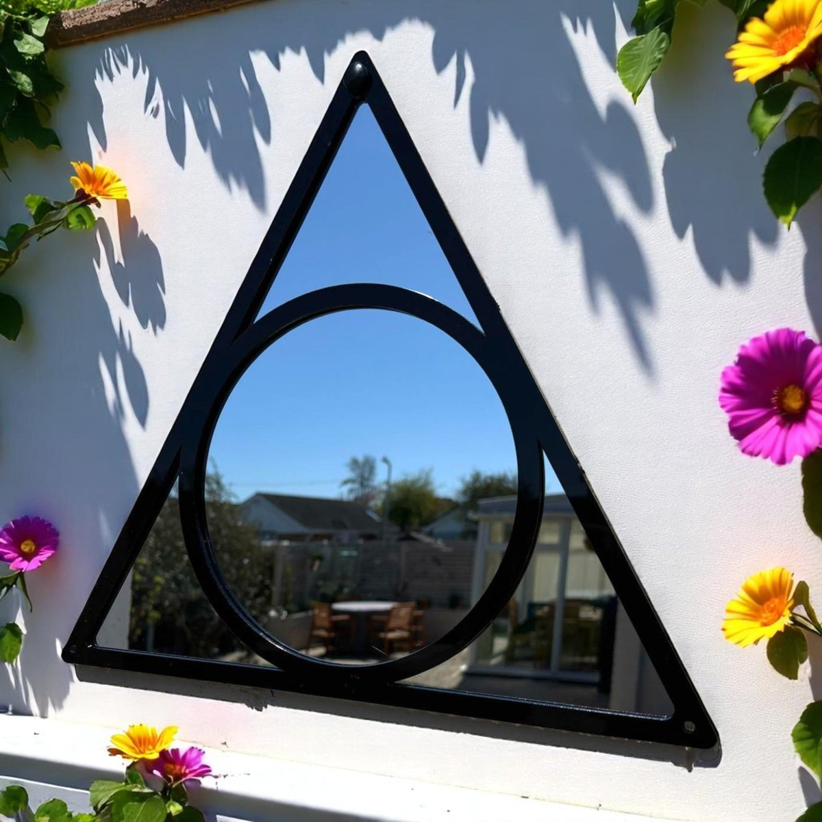A black metal garden mirror featuring an outer triangle enclosing a circle, mounted on a white wall.