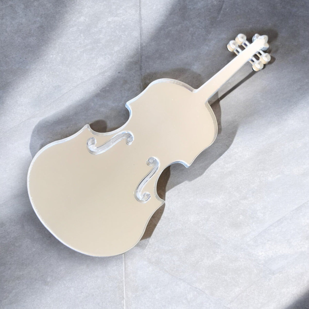 A violin-shaped silver mirror resting on a grey surface.