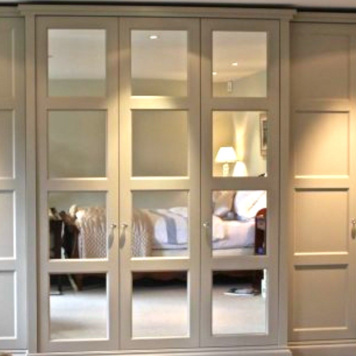 Bespoke rectangular mirrors fitted into four-panel cream wardrobe doors.