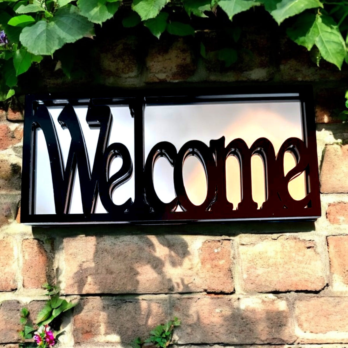Rectangular black framed garden mirror with the word 'Welcome' cut out in black script across the glass.