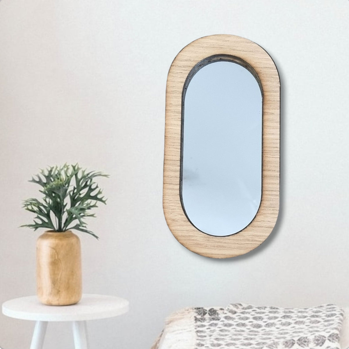 Pill-shaped mirror with a light wood frame hanging on a white wall.