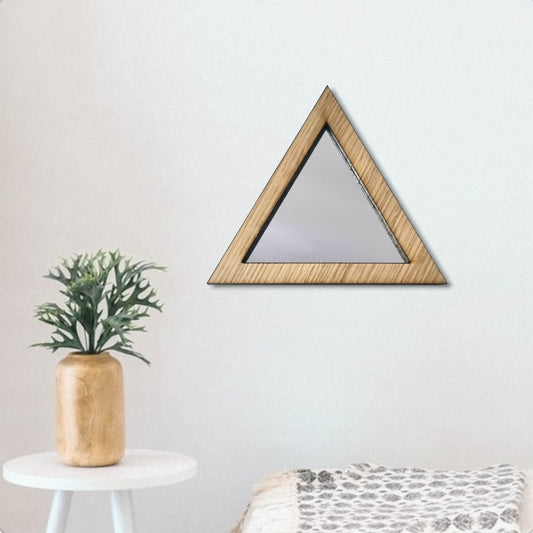 A triangular mirror with a light wood frame hangs on a white wall above a small side table and patterned blanket.